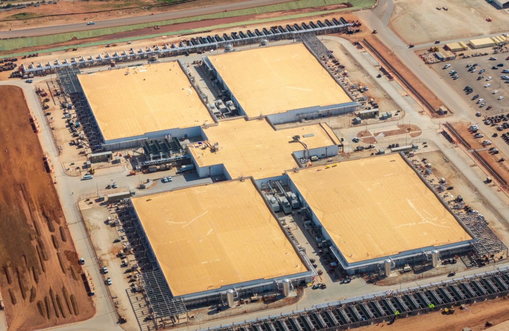 Aerial view of a large data center complex with multiple buildings and cooling equipment.
