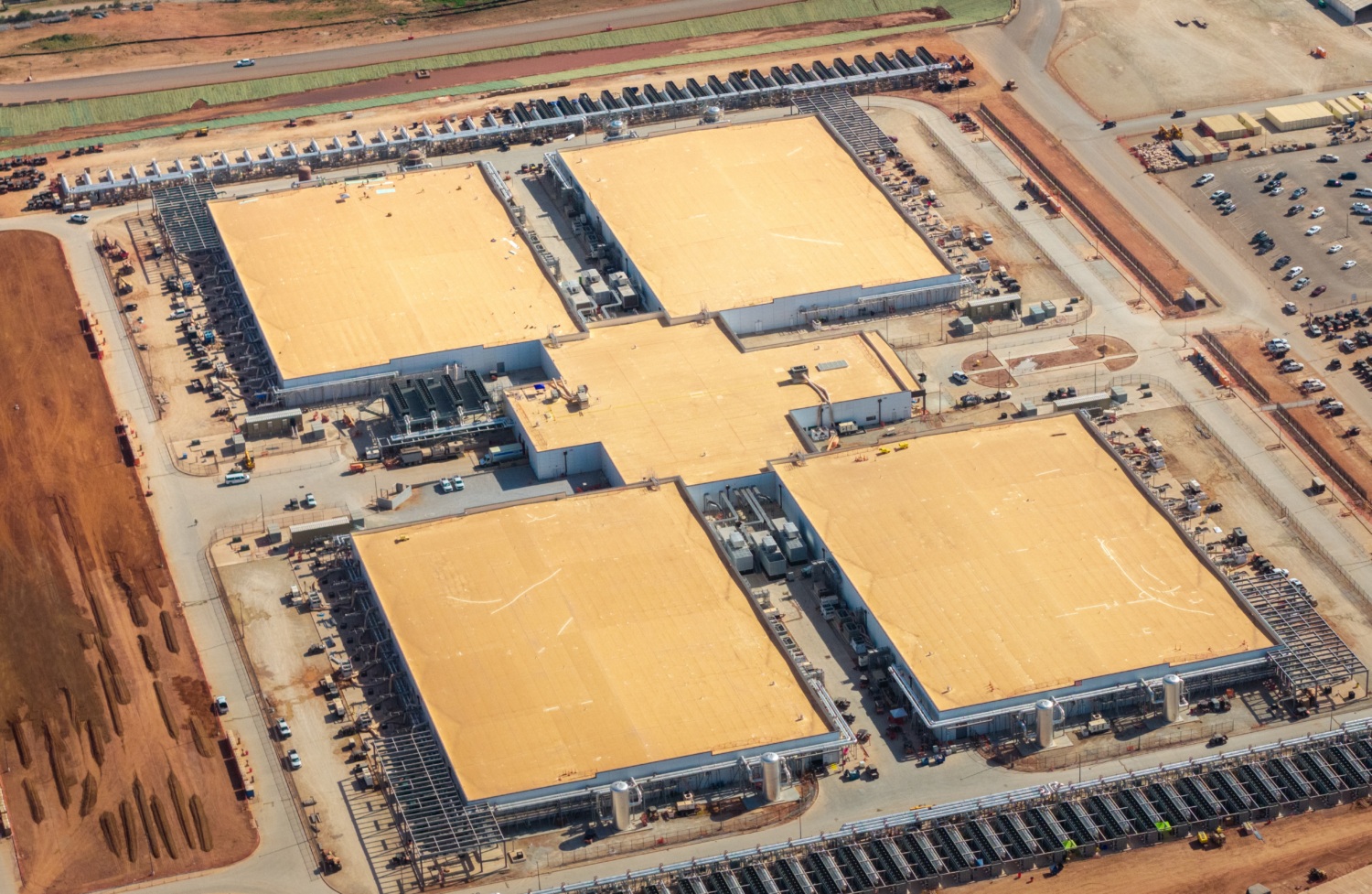Aerial view of a large data center complex with multiple buildings and cooling equipment.